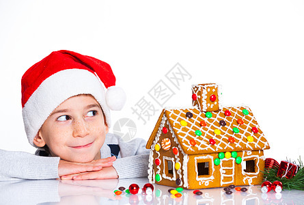 穿着圣诞老人帽子的小男孩和姜饼屋乐趣假期孩子庆典糖果食物传统蛋糕微笑幸福图片