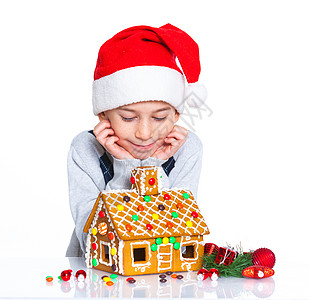 穿着圣诞老人帽子的小男孩和姜饼屋假期乐趣沙漠食物庆典传统微笑孩子幸福糖果图片