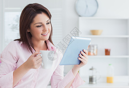 微笑的女人用咖啡杯看着数字平板电脑衬衫触摸屏女性闲暇技术女士幸福咖啡系列生命图片