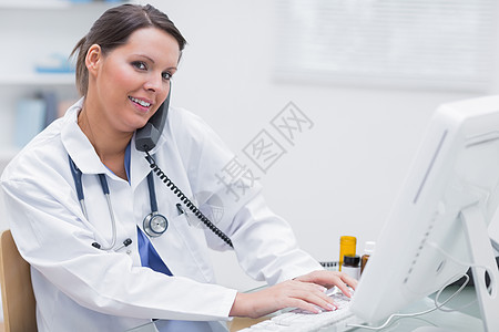 女医生在诊所待命时使用计算机的女医生电话医务室电脑从业者电脑显示器桌子女士办公室固定电话技术图片