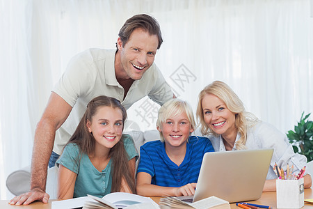 微笑的家庭使用笔记本电脑一起做功课图片