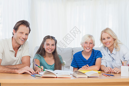 妈妈儿子微笑的父母帮助子女做功课; 在家庭作业方面背景
