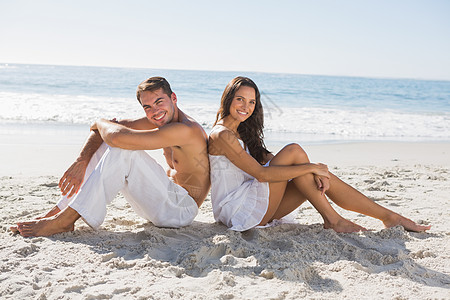 坐在沙滩上对着镜头微笑的一对情侣图片