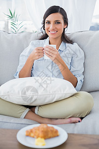 在沙发上快乐的女人 喝咖啡和吃羊角面包图片