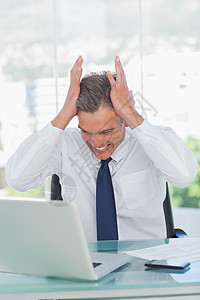 愤怒的商务人士在看笔记本电脑时用手顶着头图片