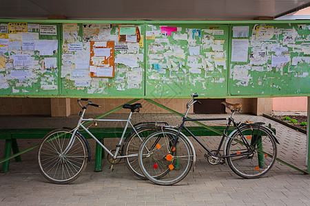 两辆旧自行车在街上对一个公告板倾斜运输民众控制板木板框架海报车轮金属踏板城市图片