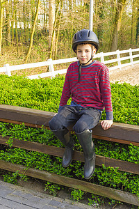 穿着头盔和靴子的可爱少年男孩 骑马坐男生速度马背木头旅行骑马牧场国家荒野骑士图片