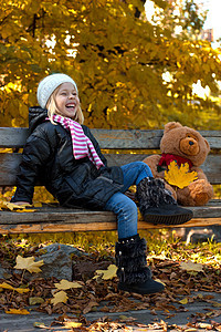 漂亮的小女孩木头幸福森林阳光金子叶子公园季节场景长椅图片