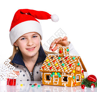 在圣诞老人帽子的女孩 与姜饼屋微笑乐趣蛋糕沙漠传统饼干糖果孩子假期庆典图片