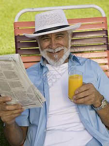 坐在草坪主席的高级男子拿着报纸和橘色果汁高观景肖像图片