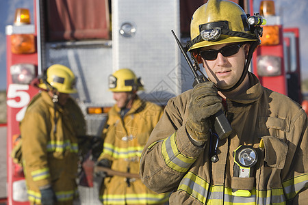 一名中年消防员的肖像 在电台与站在背景的同事交谈时讲话;他们站在这里图片