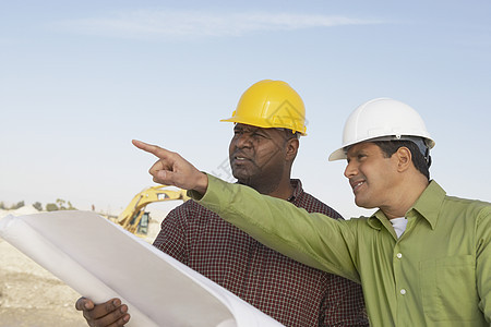 两名多族裔建筑工人 在工地用蓝图对着天空全体手指男人帽子拉丁男士安全帽衬衫工作经理图片