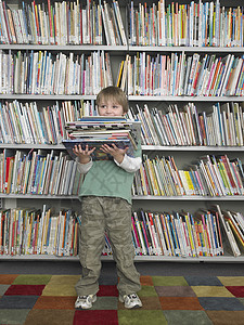 整个快乐的年轻男孩在图书馆里持有一堆书图片