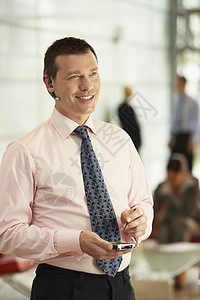 中年商务人士与背景同事在办公室使用蓝牙 同时用手机做客的中年生意人;图片