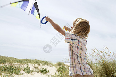 在风沙滩上放风筝的 青春期前男孩的侧边视景图片