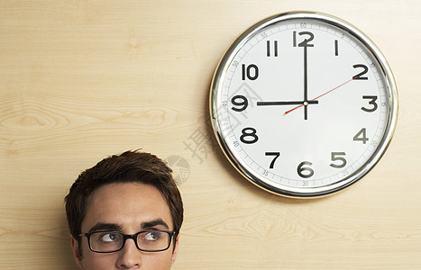 年轻商务人士戴眼镜看办公室木墙上时钟的头像图片