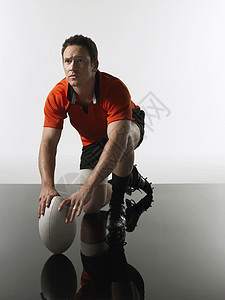 橄榄球运动员跪在膝上握着球背景图片