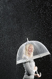 一位微笑的女商务人士在雨中站在雨伞下站着的侧面肖像图片