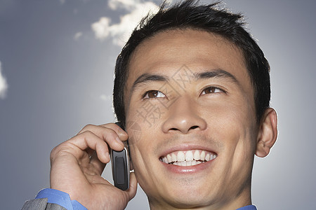一个微笑的年轻商务人士在天空下使用手机的特写图片