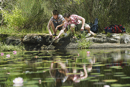 两个十几岁的男孩 蹲在湖边 一个把棍子放进水里图片