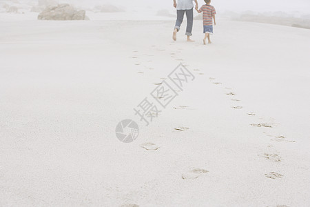 父亲和儿子在海滩沙滩上留下脚印后行走的近视图片