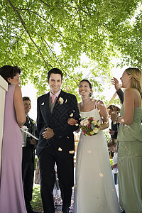 新娘和新郎走在路上 人们向空气中投掷花瓣小群人风俗花束享受活动燕尾服婚礼婚纱团结海关图片