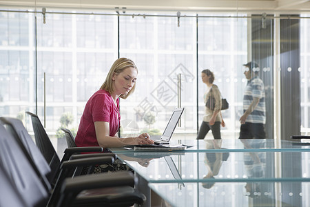 女办公室工作人员在同事通过会议室时使用手提笔记本电脑椅子女性成人专注房间玻璃反射职场商业女士图片