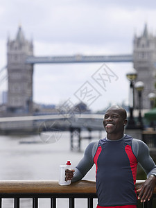 在英格兰塔桥前 拿着水瓶微笑着年轻非裔美国人男子的笑容肌肉闲暇赛跑者思维瓶子锻炼享受运动男人建筑学图片