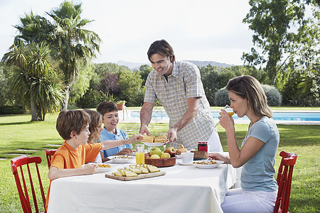 三人和三个孩子一起在户外早餐桌旁坐着图片