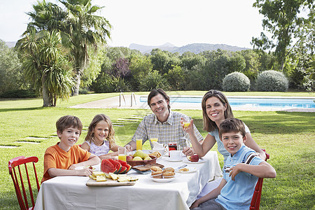 一对微笑的情侣的肖像 有三个孩子坐在花园的早餐桌前吃早餐图片