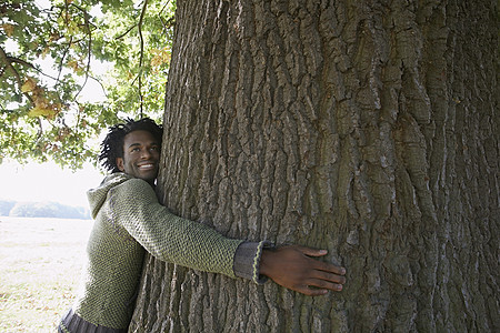 快乐的非洲裔美国男人在公园边拥抱树干时 却望着远看图片