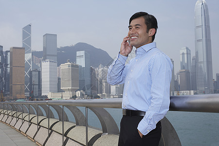 快乐的年轻商务人士在桥上使用手机与背景城市风景相联图片