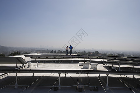 维修工人站在加州洛杉矶屋顶的太阳能电池阵列上 并站立在一起男人风景戏剧性发电成人两个人环境问题男性能源蓝天图片