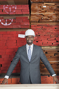 快乐的非洲裔美国男性承包商的肖像 其背景是堆叠木木板图片