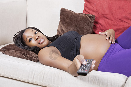 年轻孕妇躺在沙发上看电视的年青孕妇图片