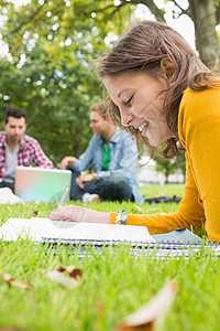 在公园使用笔记本电脑与男生一起写学生笔记男人学习说谎朋友们头发家庭作业写作大学学校草地图片