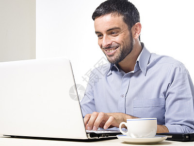 与胡子一起的年轻人在笔记本电脑上工作杯子冲浪桌子公司键盘蓝色商务男人职场人士图片
