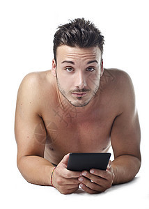 英俊帅气的青年男子不穿衬衫 在地板上阅读电子书触摸屏屏幕微笑成人地面技术软垫男人肌肉电脑图片