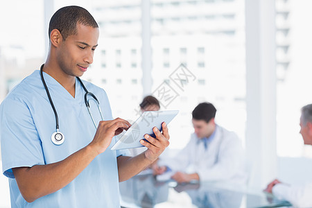 使用数字平板电脑 在医院的桌子周围组群进行外科手术诊所医生女性雇员触摸屏职场团体从业者工人会议图片