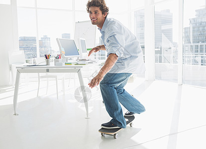 快乐的年轻人在办公室滑板商业职场牛仔布屏幕桌子微笑电脑工作男性技术图片