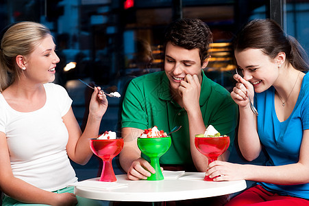 三个朋友享受着美味的甜点微笑勺子诱惑女孩三重奏快乐盘子青少年浇头餐厅图片