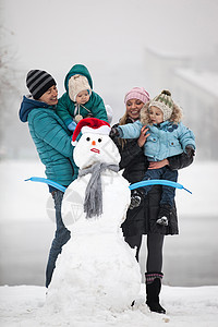 有两个儿子的年轻家庭在户外雪人旁边图片