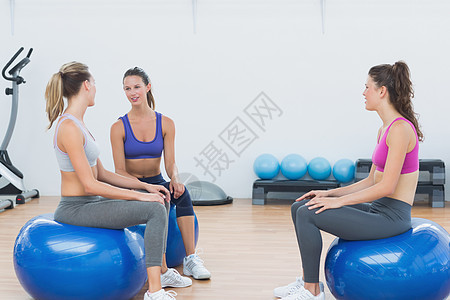 坐在运动球上运动的年轻体育女青年训练调子运动员运动服文胸健身室朋友们平衡健身房健身图片