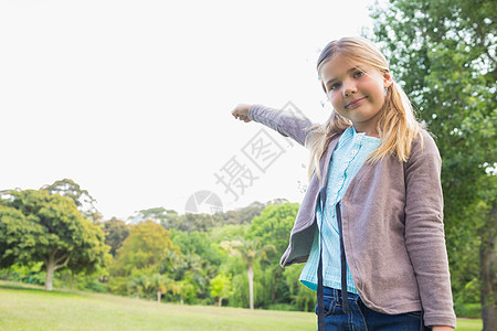 可爱笑笑的年轻女孩站在公园绿色浅色幸福天空微笑金发女郎童年手势喜悦乐趣图片