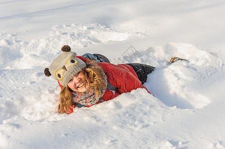 女孩在雪中玩帽子说谎女性喜悦微笑女士红色雪堆空翻乐趣图片