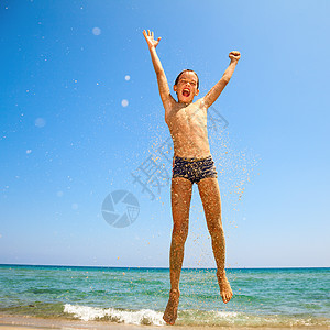 男孩在海滩上跳跃男生享受晴天闲暇活力喜悦棕褐色孩子游泳衣乐趣图片
