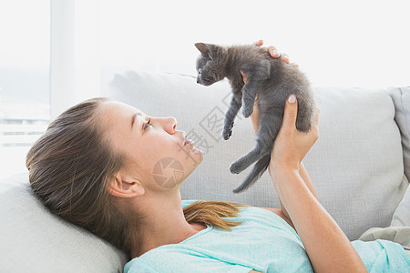躺在沙发上 抱着一只灰小猫的开心女人图片