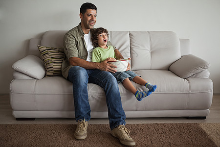 父亲和儿子在客厅里 拿着爆米花碗看电视软垫男性团结枕头孩子房子娱乐小地毯家庭成人图片