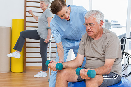 女理疗师协助老年男子使用哑铃训练男性人员医务室起重运动服健身房健身工具治疗图片