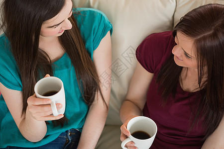两个笑笑的朋友在沙发上喝咖啡和聊天图片